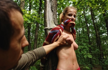 Petite blonde girl is flogged while tied to a tree in the forest
