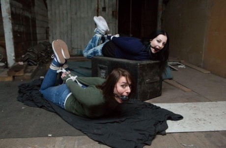 Two white girls are hogtied and ball gagged in sweaters and jeans