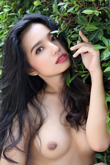 Beautiful Asian girl Norah gets totally naked next to a hedge in a garden