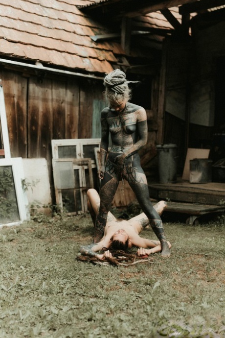 Heavily tattooed girls piss on a naked man outside the back steps of a house
