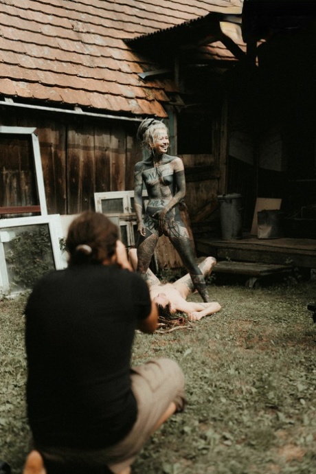 Heavily tattooed girls piss on a naked man outside the back steps of a house