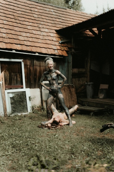 Heavily tattooed girls piss on a naked man outside the back steps of a house