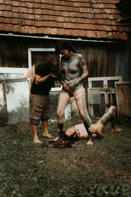 Heavily tattooed girls piss on a naked man outside the back steps of a house
