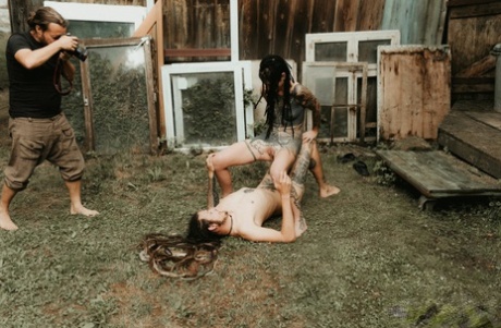 Heavily tattooed girls piss on a naked man outside the back steps of a house