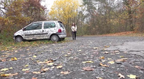 White girl Nicolette Noir takes a piss beside a parked car in a wooded setting