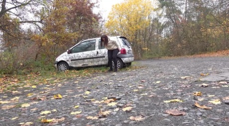 White girl Nicolette Noir takes a piss beside a parked car in a wooded setting