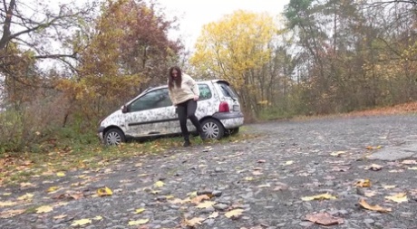 White girl Nicolette Noir takes a piss beside a parked car in a wooded setting