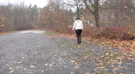 White girl Nicolette Noir takes a piss beside a parked car in a wooded setting