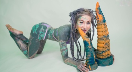 Heavily tattooed girl Anuskatzz holds a couple of taintacle toys in the nude