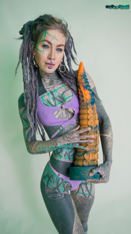 Heavily tattooed girl Anuskatzz holds a couple of taintacle toys in the nude