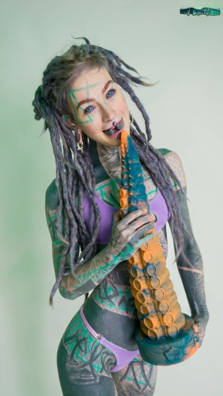 Heavily tattooed girl Anuskatzz holds a couple of taintacle toys in the nude