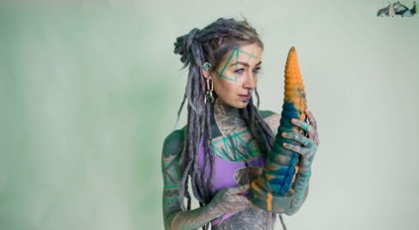 Heavily tattooed girl Anuskatzz holds a couple of taintacle toys in the nude